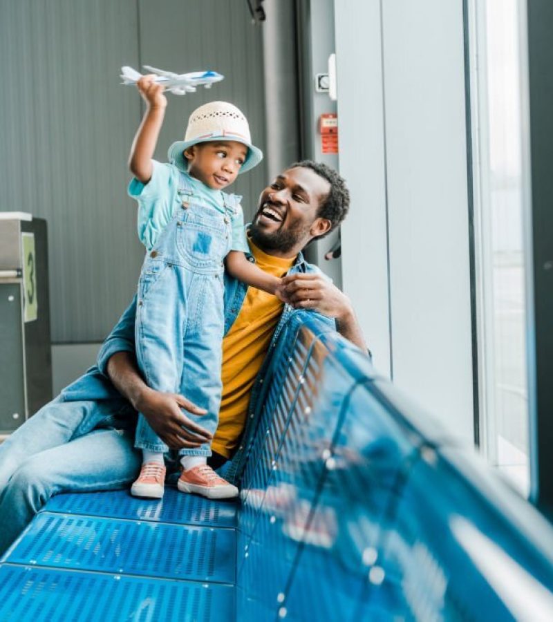 happy african american father looking at son while boy playing with toy plane in airport