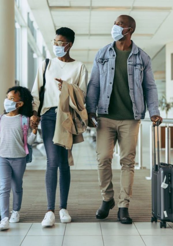 Tourist family walking through passageway in airport. Young girl with family in face masks walking with luggage in airport corridor.